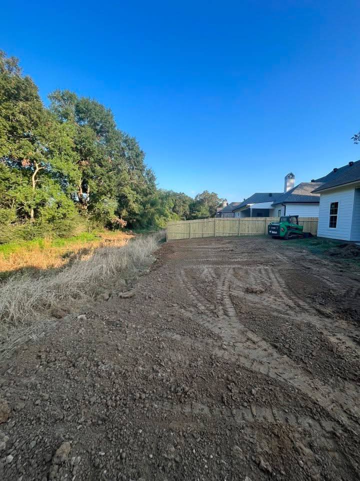 Graded backyard lot behind a home with a skid steer, ready for the next phase of a land preparation project