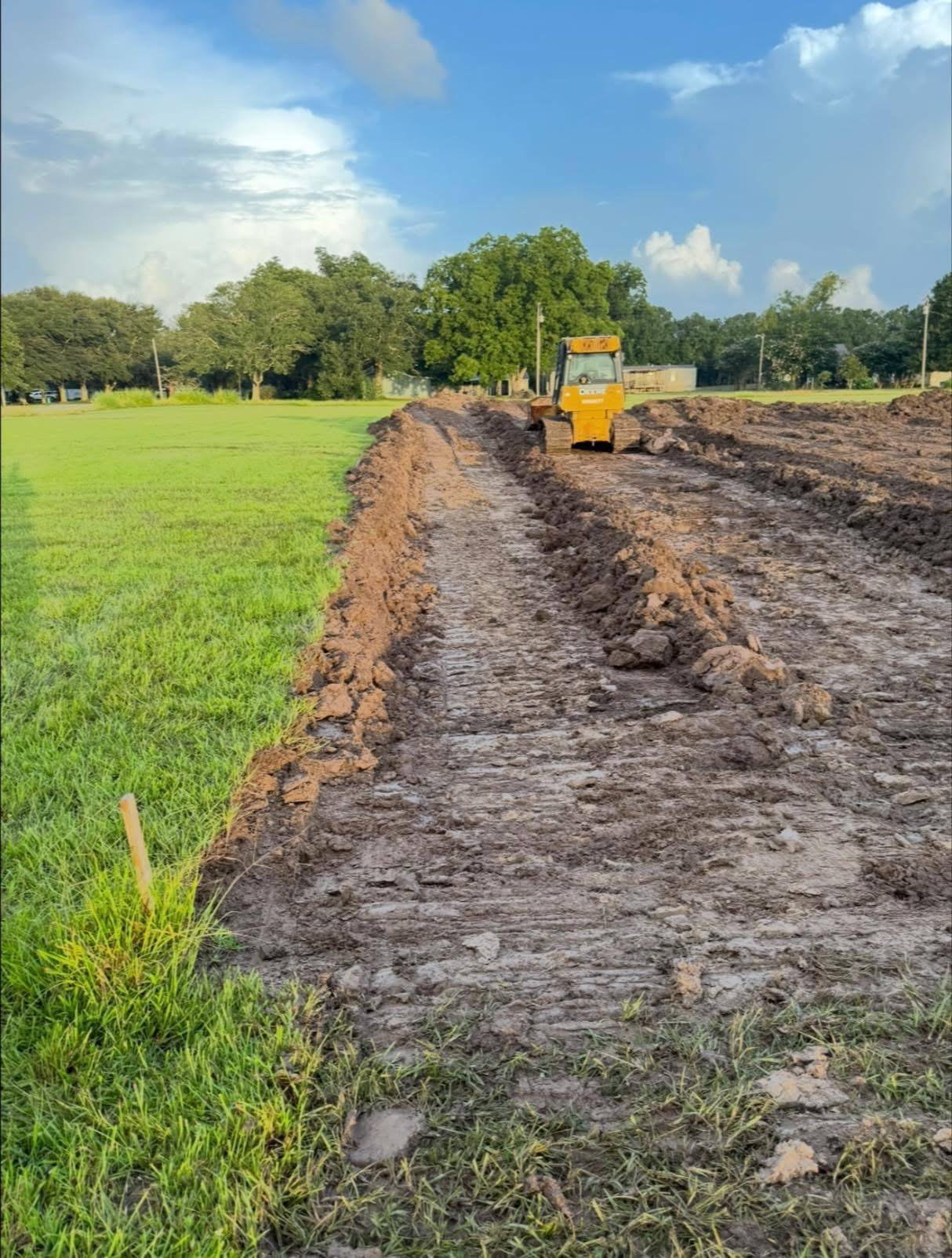 Bulldozer pushing dirt to grade a large open field for a South Louisiana land preparation project