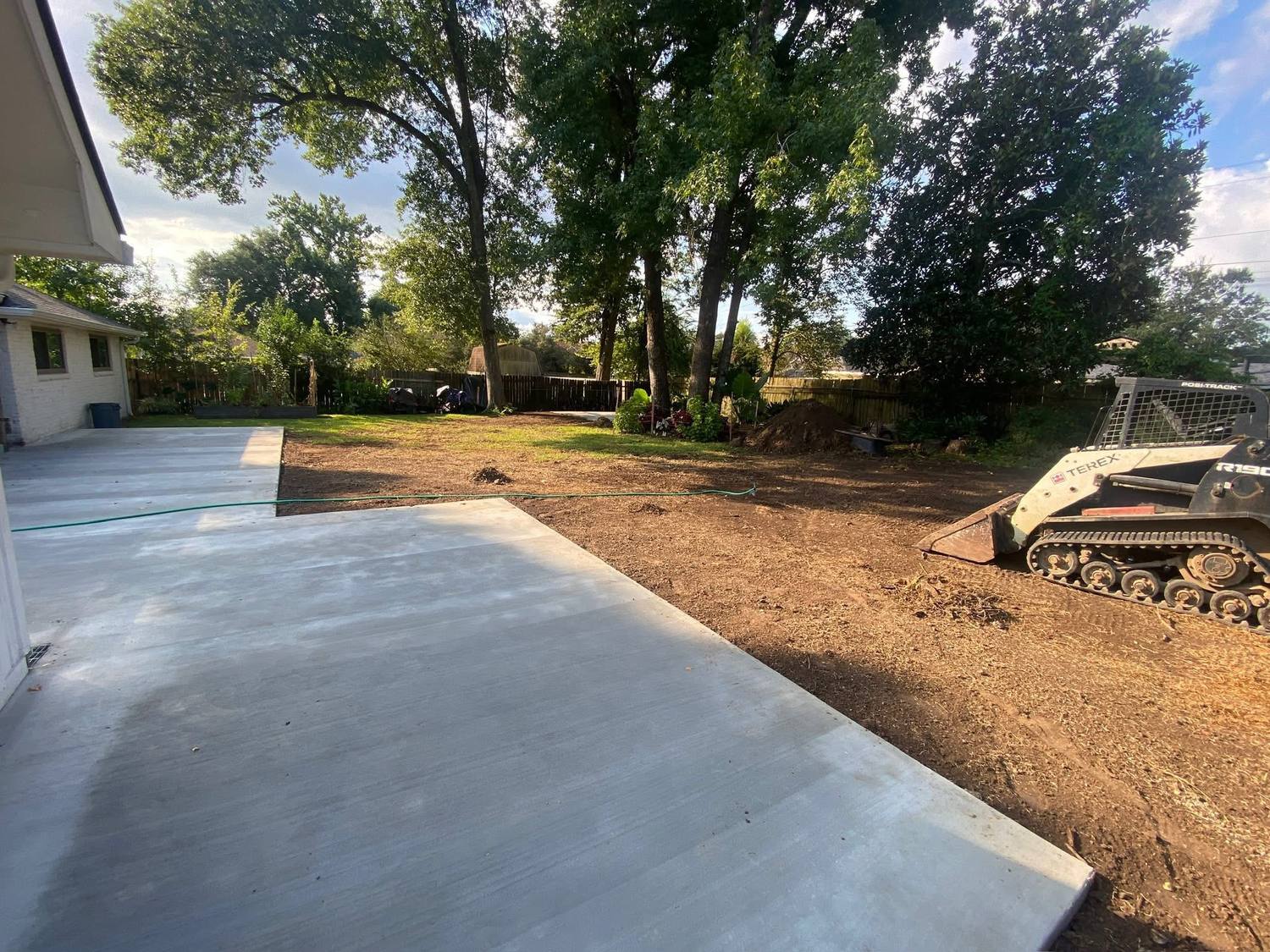 Freshly poured concrete pad next to graded dirt with a skid steer on a residential job site