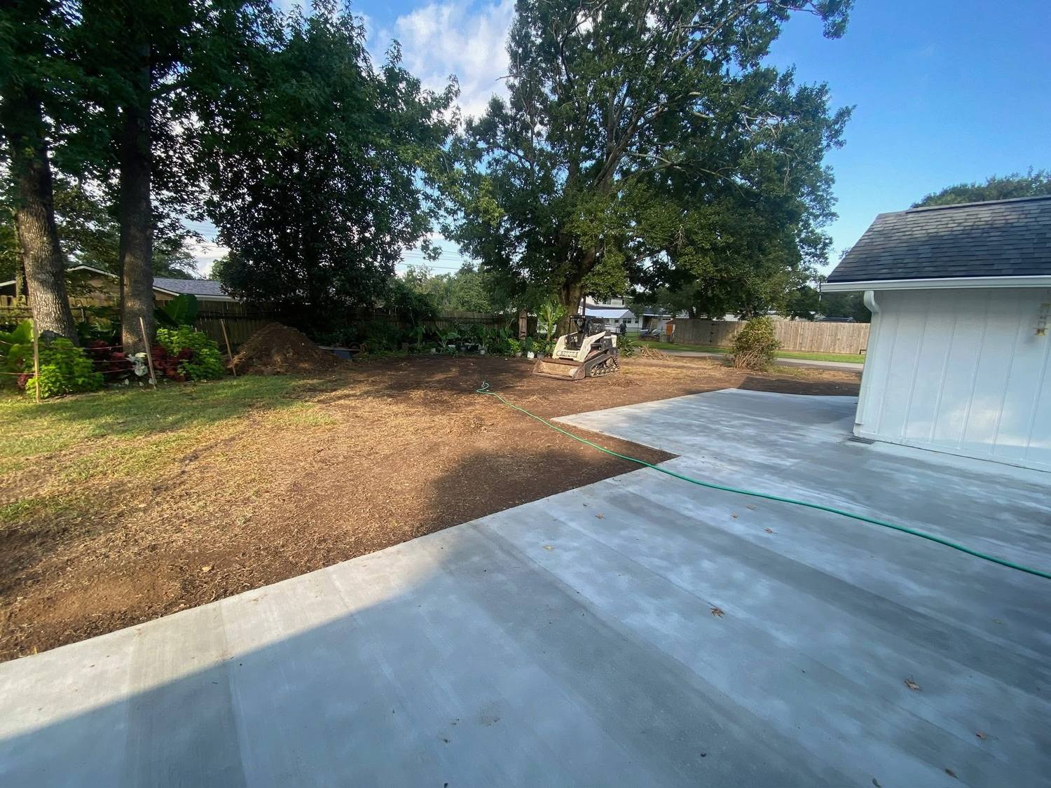 Graded dirt and concrete pad behind a home with equipment staged on site